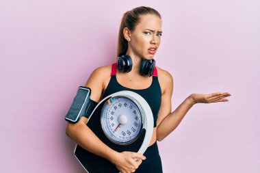 Güzel sarışın spor kadın kilo verme ve kafası karışık yüz ifadesini dengelemek için kilo makinesini tutuyor. şüphe kavramı. 