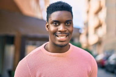 Genç Afrikalı Amerikalı adam gülümseyerek şehirde mutlu mesut duruyor..