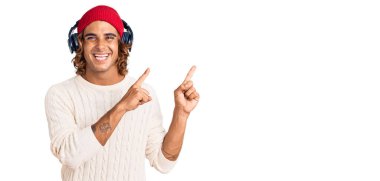 Genç İspanyol adam müzik dinliyor kulaklık takıyor gülümsüyor ve kameraya bakıyor iki eliyle ve parmaklarıyla kenarı işaret ediyor.. 