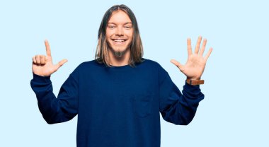 Uzun saçlı yakışıklı beyaz adam günlük kışlık süveter giyiyor ve yedinci parmaklarını gösterip gülümsüyor ve mutlu.. 