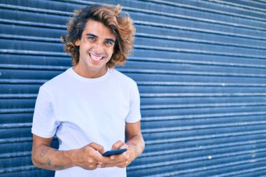 Şehrin caddesinde akıllı telefon kullanan, mutlu gülümseyen genç İspanyol adam.