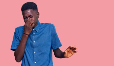 Genç, Afro-Amerikan bir adam günlük giysiler giymiş pis ve iğrenç bir koku alıyor, dayanılmaz bir koku, parmakları burnunda nefesini tutuyor. Kötü kokuyor. 