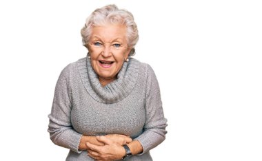 Kış süveteri giyen yaşlı, gri saçlı bir kadın. Gülümsüyor ve kahkahalarla gülüyor. Çünkü elleri vücutta olan komik bir şaka.. 