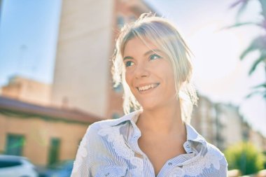 Genç sarışın kadın gülümseyerek şehirde mutlu mesut yürüyor..