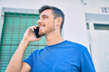 Genç beyaz adam gülümsüyor. Şehirdeki akıllı telefondan konuşuyor..