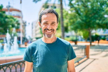 Orta yaşlı, sakallı, açık havada mutlu gülümseyen bir adam.