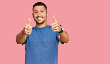 Dövmeleri olan, günlük giysiler giyen, olumlu jestler yapan, gülümseyen ve başarı için sevinen yakışıklı bir adam. kazanan jest. 