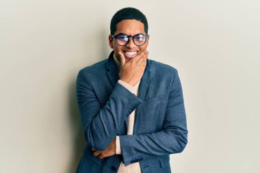 Zarif kıyafetler giyen ve gözlüklü yakışıklı genç adam kameraya kendinden emin bir şekilde bakıyor kollarını kavuşturmuş ve çenesini kaldırmış gülümsüyor. Olumlu düşünmek. 