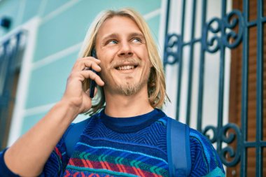 Genç İskandinav öğrenci gülümsüyor. Şehirdeki akıllı telefondan mutlu bir şekilde konuşuyor..