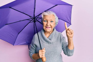 Yaşlı, gri saçlı, elinde mor şemsiyeyle gülümseyen bir kadın. Bir numaralı mutlu yüzle işaret eden bir fikir ya da soru. 