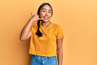 Gündelik kıyafetler giyen, gülümseyen, el ve parmaklarıyla telefon hareketi yapan, telefonda konuşan genç Latin bir kadın. iletişim kavramları. 