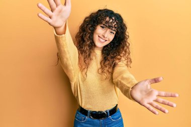 Gündelik giysiler giymiş genç İspanyol kız kameraya sarılmak için kollarını açmış gülümseyerek bakıyor. Mutluluğu kucaklayan neşeli bir ifade.. 