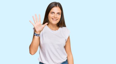 Beyaz günlük tişörtler giyen genç beyaz kadın beş numarayı gösterip işaret ederken kendinden emin ve mutlu bir şekilde gülümsüyor.. 