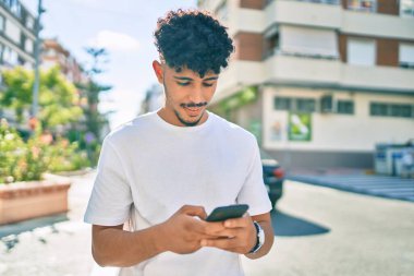 Genç Arap adam şehirde akıllı telefon kullanarak mutlu bir şekilde gülümsüyor..