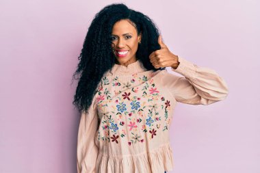 Orta yaşlı Afro-Amerikalı kadın günlük kıyafetler giyiyor mutlu ve pozitif gülümsüyor, başparmağıyla mükemmel ve onay işareti yapıyor. 