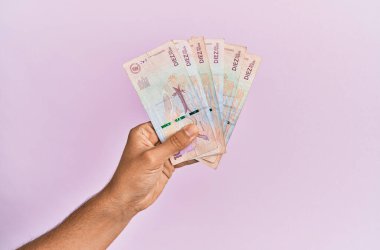 İspanyol el, izole edilmiş pembe arka planda 10 Kolombiya pezosu tutuyor..