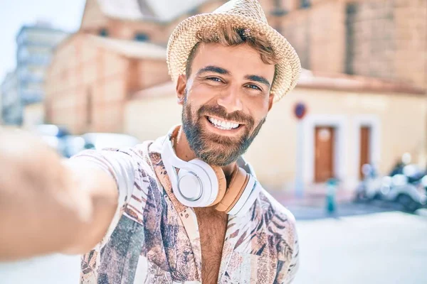 Tatilde olan genç İspanyol adam kulaklık takıyor ve şehrin caddesindeki kamerada selfie çekiyor.