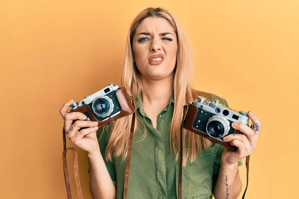 Young caucasian woman holding vintage camera clueless and confused expression. doubt concept.
