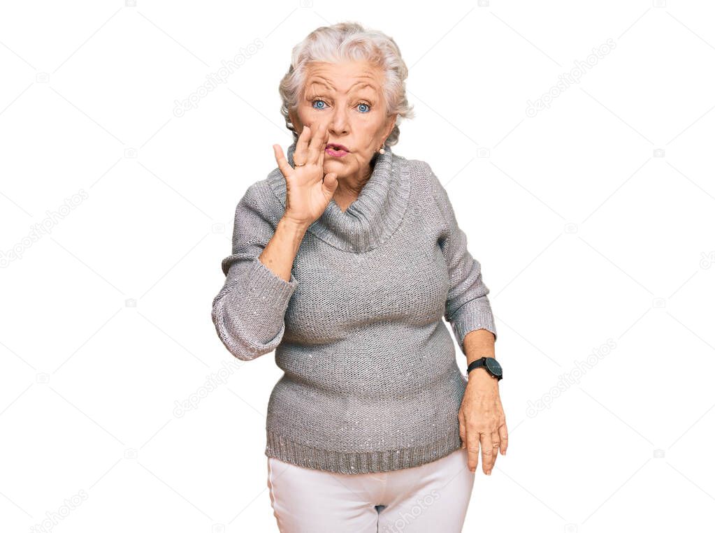 Senior grey-haired woman wearing casual winter sweater hand on mouth telling secret rumor, whispering malicious talk conversation 