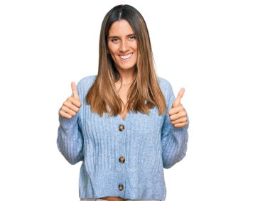 Gündelik kıyafet giyen genç bir kadın. Başarı işareti yapıyor. Elleriyle olumlu jest yapıyor. Neşeli ifade ve kazanan jest. 