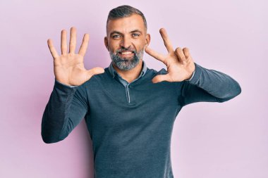 Orta yaşlı, sıradan kıyafetler giyen yakışıklı bir adam sekiz numaralı parmaklarıyla gülümseyerek mutlu ve kendinden emin bir şekilde onu işaret ediyor.. 