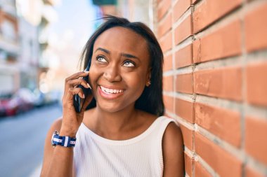 Genç Afrikalı Amerikalı kadın gülümsüyor. Şehirdeki akıllı telefondan mutlu bir şekilde konuşuyor..