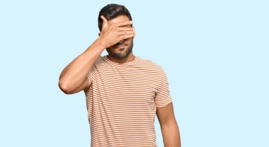 Yakışıklı İspanyol bir adam, günlük kıyafetler giyiyor, gözlerini eliyle kapatıyor, ciddi ve üzgün görünüyor. Görme, saklama ve reddetme konsepti 