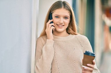 Kafkasyalı güzel bir genç şehirde kahve içerek akıllı telefondan konuşuyor..