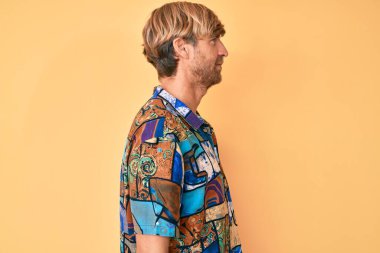 Yazlık tişört giyen genç sarışın adam yan yan bakıyor, rahat poz veriyor doğal bir yüz ve kendine güvenen bir gülümseme.. 