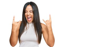 Genç ve güzel İspanyol bir kız, günlük kıyafetler giyip çılgın bir ifadeyle bağırıyor ve elleri havada rock sembolü yapıyor. Müzik yıldızı. ağır kavram. 