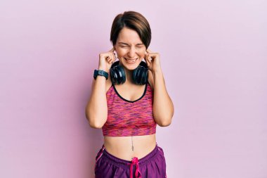 Kısa saçlı, spor giyimli, kulaklık takan, kulaklık takan ve yüksek sesli müzik sesi için rahatsız edici ifadeleri olan genç esmer kadın. sağır kavramı. 