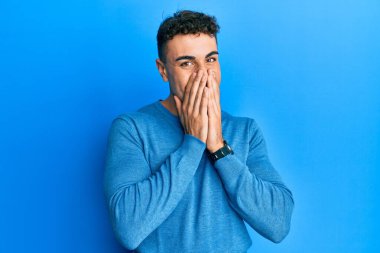 Kış süveteri giyen İspanyol genç adam gülüyor ve utanıyor kıkırdıyor elleriyle ağzını kapatıyor, dedikodu ve skandal konsepti yapıyor. 