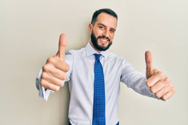 Sakallı genç adam iş kravatı takıyor. Elleriyle olumlu bir jest yapıyor. Gülümsüyor ve başarı için seviniyor. kazanan jest. 