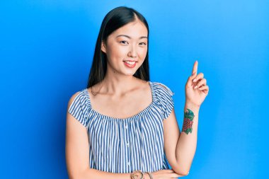 Yüzünde kocaman bir gülümseme olan sıradan çizgili tişört giyen genç Çinli kadın, kameraya el ve parmak ile bakıyor.. 