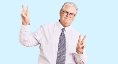 İş kıyafetleri giymiş, gülümseyen, parmaklarını zafer işareti yaparken gösteren yaşlı gri saçlı adam. İki numara.. 