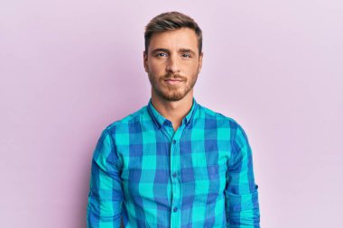 Yüzünde ciddi bir ifade olan günlük kıyafetler giyen yakışıklı beyaz bir adam. Basit ve doğal bir şekilde kameraya bakıyorsun.. 