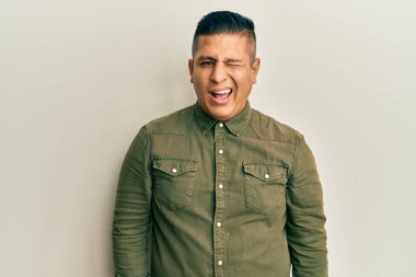 Gündelik kıyafetler giyen genç Latin adam kameraya seksi bir ifadeyle bakıyor, neşeli ve mutlu bir yüzle.. 