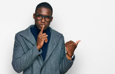 İş kıyafetleri ve gözlük takmış genç Afro-Amerikalı adam sessiz olmak istiyor. Parmakları dudaklarında, elleri yandan işaret ederek. sessizlik ve gizli konsept. 