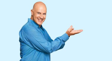 Orta yaşlı, kel bir adam, sıradan kıyafetler giymiş, avuçlarını açmış, fotokopi alanını gösteren, gülümseyerek mutlu bir gülümseme sunan, 