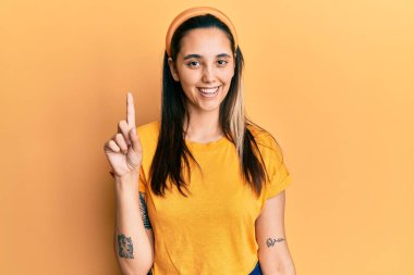 Sarı bir tişört giyen genç İspanyol kadın bir fikir veya soruyla gülümsüyor ve mutlu bir yüzle işaret ediyor. 