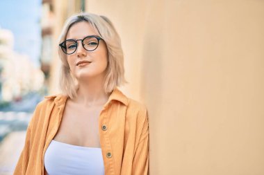 Genç sarışın kız gülümsüyor, şehirde gözlük takıyor..