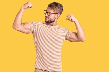 Sıradan kıyafetler ve gözlük takan genç beyaz bir adam gururla gülümseyen kol kaslarını gösteriyor. fitness konsepti. 