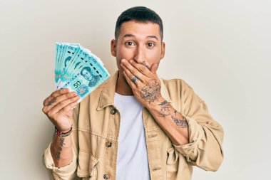 50 Yuan 'lık Çin banknotları tutan yakışıklı bir adam ağzını eliyle kapatıyor, şok geçiriyor ve hata yapmaktan korkuyor. şaşırmış ifade 
