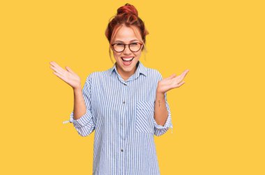 Genç kızıl saçlı kadın gündelik kıyafetler ve gözlük takıyor zaferi mutlu bir gülümsemeyle kutluyor ve kazanan yüz ifadesi kaldırıyor. 