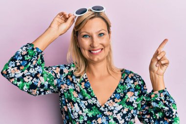 Orta yaşlı, beyaz, çiçekli gömlek ve güneş gözlüğü takan bir kadın gülümsüyor. 