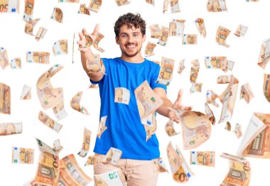 Kıvırcık saçlı, sıradan giyinmiş, kameraya bakıp sarılmak için kollarını açmış gülümseyen genç, yakışıklı bir adam. Mutluluğu kucaklayan neşeli bir ifade..