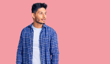 Yakışıklı Latin Amerikalı rahat gömlekler giyen genç adam yüzünde gülümsemeyle yan yana bakıyor, doğal bir ifade. Kendinden emin gülen. 