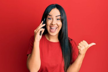 Genç, güzel, İspanyol bir kız akıllı telefondan konuşuyor. Parmağını kaldırıyor, gülümsüyor, ağzı açık. 