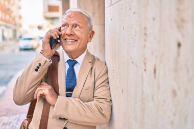 Kıdemli gri saçlı işadamı gülümsüyor. Şehirdeki akıllı telefondan mutlu bir şekilde konuşuyor..