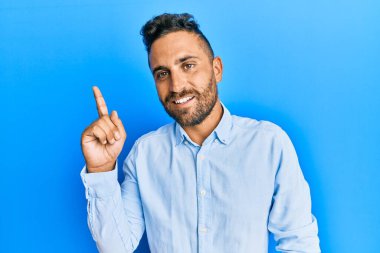Sakallı, sıradan kıyafetler giyen yakışıklı bir numaralı parmağı gösterip işaret eden, kendinden emin ve mutlu gülümseyen adam.. 